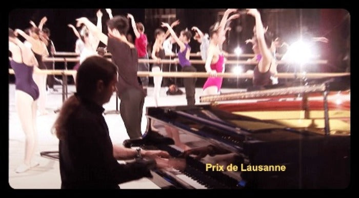 A concert scene with a pianist seated at a grand piano in the foreground, while a ballet class or rehearsal fills the background with dancers raising their arms. Bright stage lighting creates glare, and the text 'Prix de Lausanne' appears in the lower right.